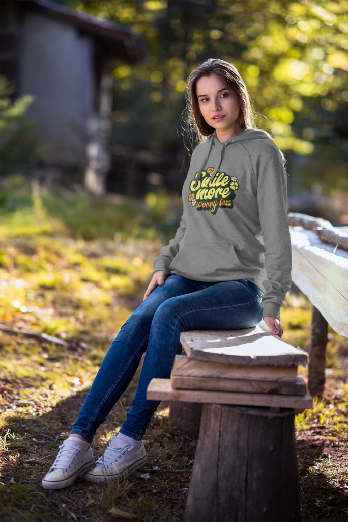 Woman wearing a hoodie with text sitting on a wooden bench outdoors.